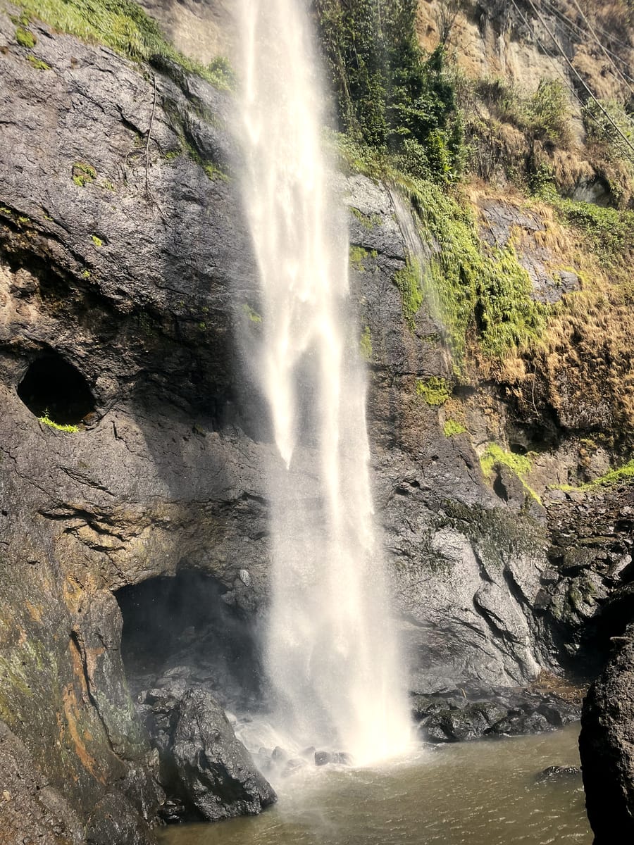 A single waterfall column at Sipi dropping past an overhanging basalt cliff.